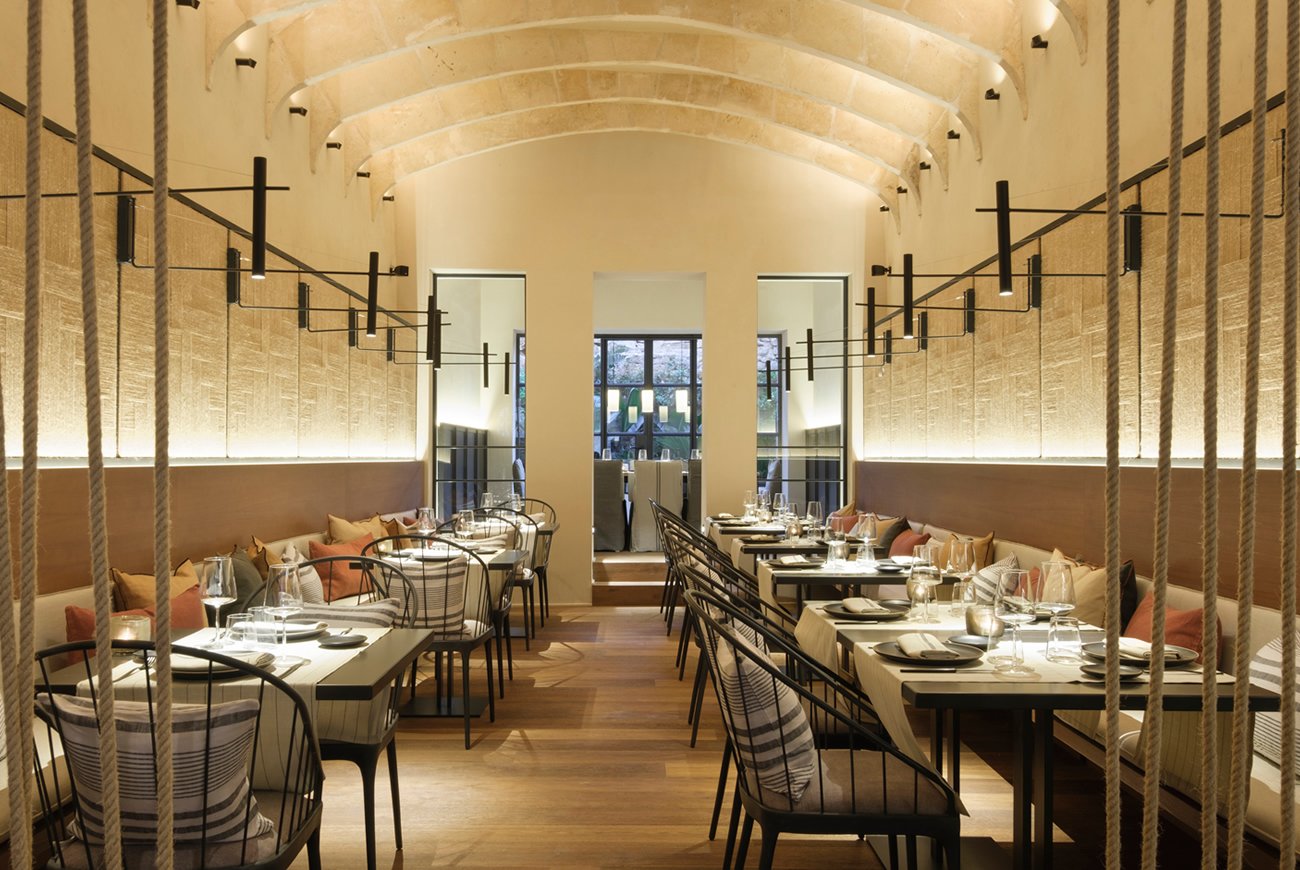 Restaurant unter einer Gewölbedecke mit hellen Tischen und dunklen Stühlen