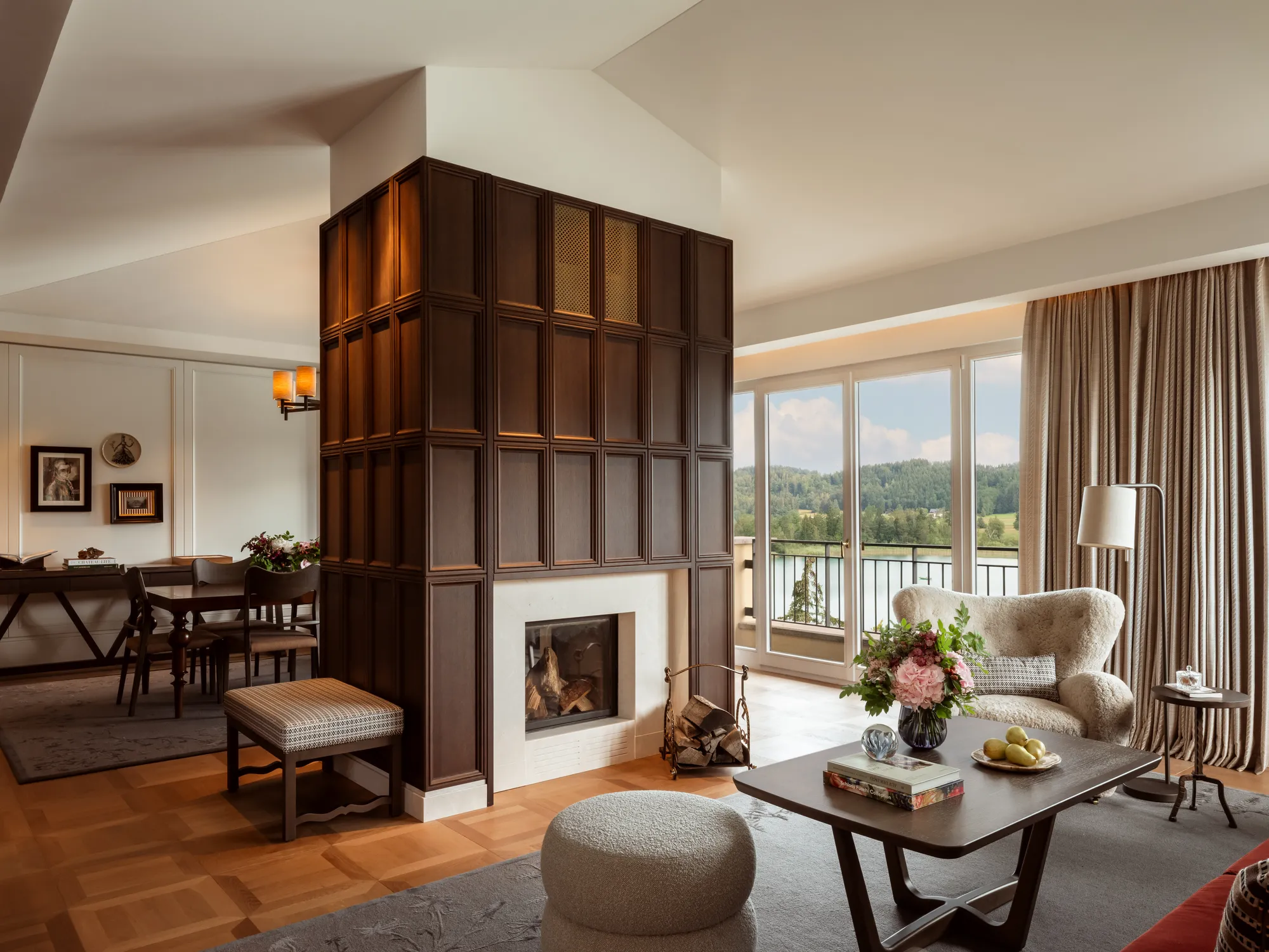 Wohnraum der Kaiser-Franz-Josef-Suite im Rosewood Schloss Fuschl mit holzverkleidetem Kamin, Kaminfeuer und Fenstern zum See