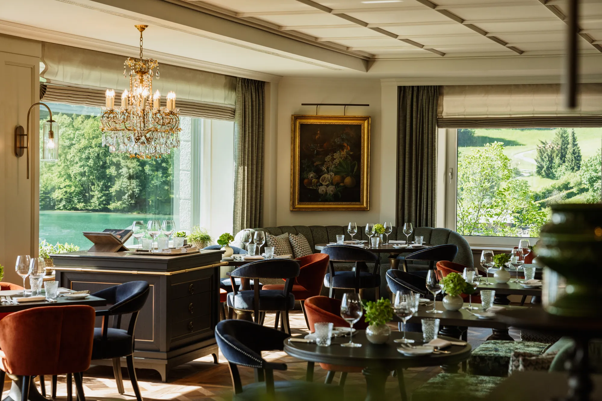 Speiseraum des Schloss Restaurants mit Kristalllüster, Samtstühlen in Rot und Blau und Fenstern zum Fuschlsee