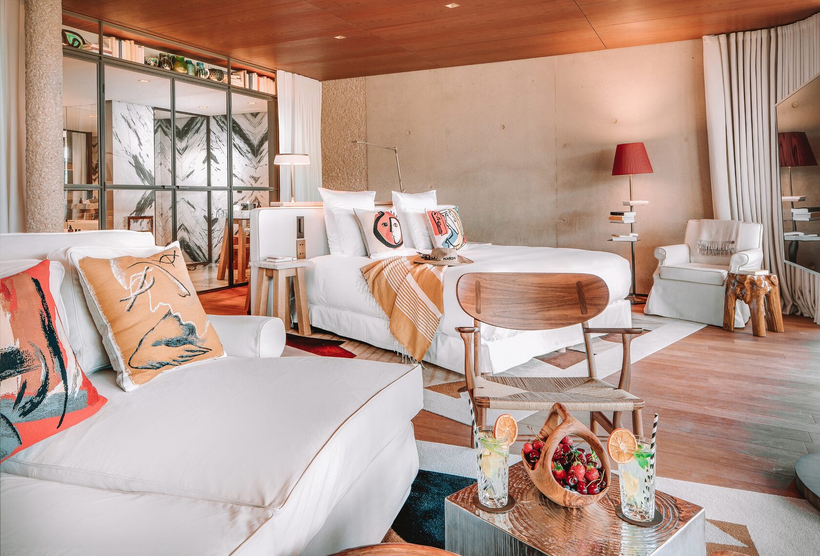 Suite in warmem Holz mit weissen Sofas, Kunstkissen und offenem Marmorbad
