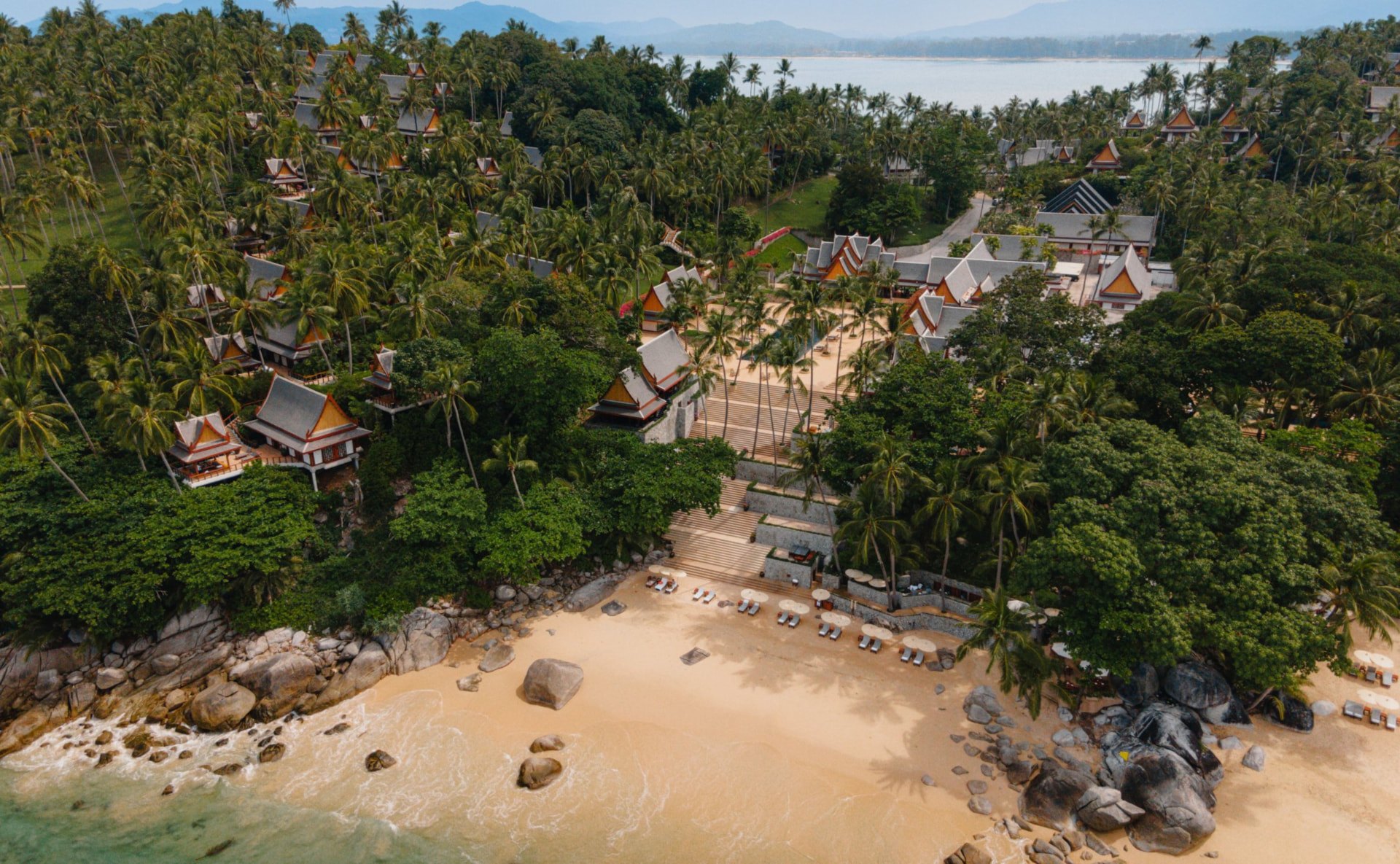 Luftaufnahme des Resorts: Dächer zwischen Kokospalmen, eine breite Treppe zum Strand und die Andamanensee
