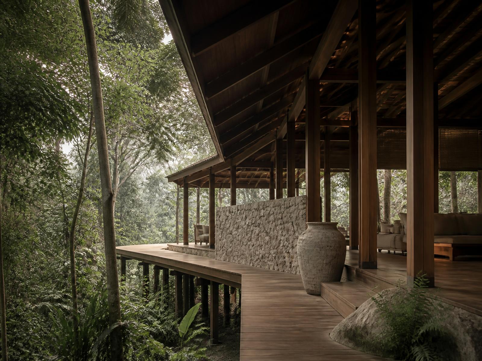 Open-air timber and natural stone pavilion with deep eaves and an elevated walkway disappearing into Malaysian rainforest