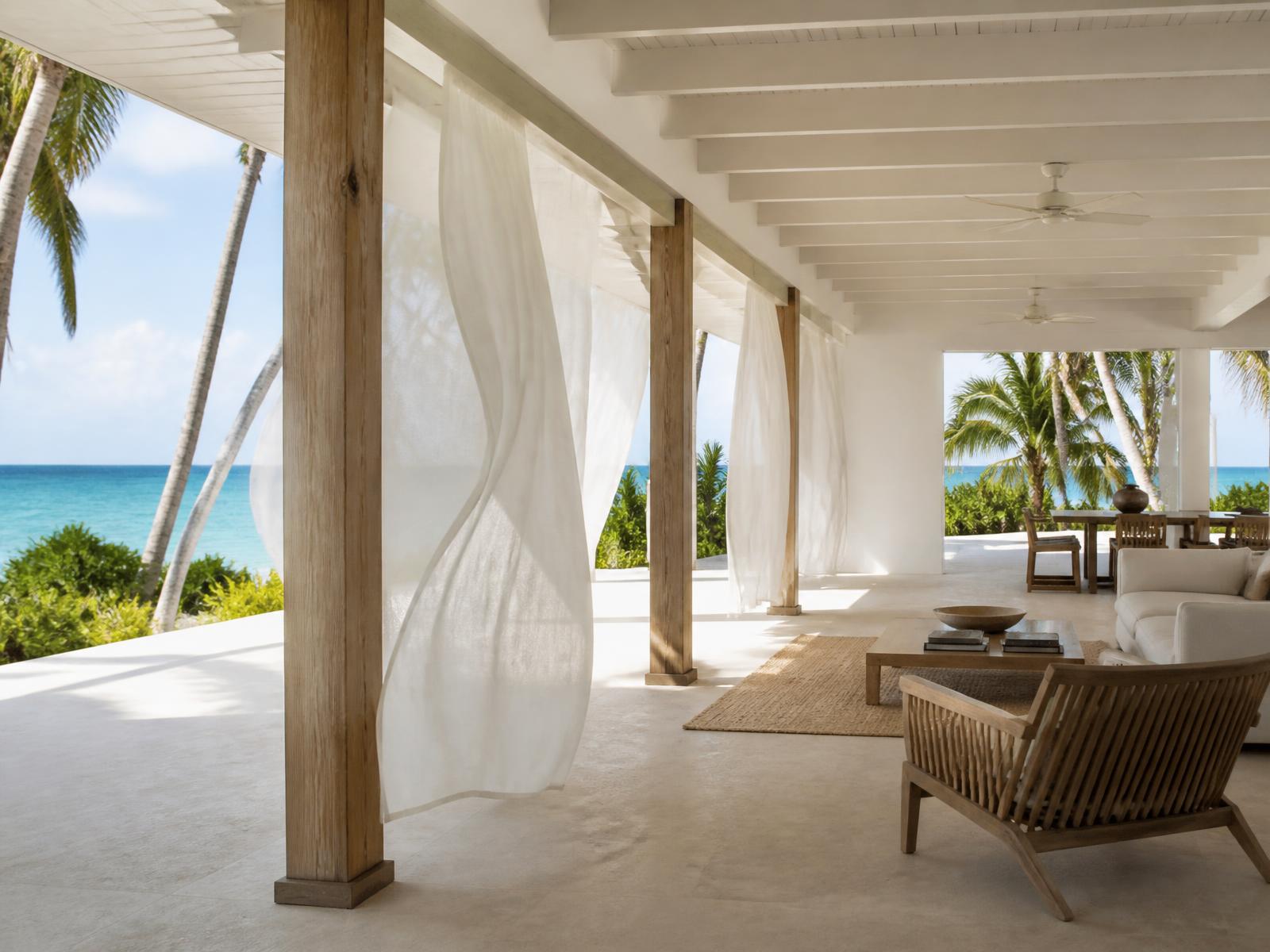 Whitewashed open-air Caribbean pavilion with teak columns, linen curtains lifting in the breeze and a view to turquoise sea