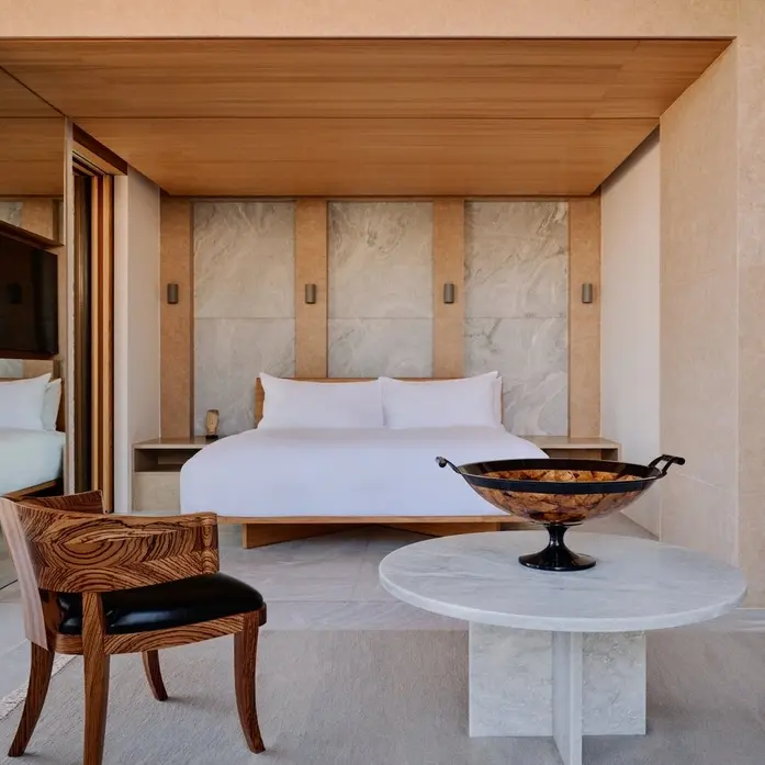 Schlafbereich einer Amanzoe-Villa mit Holzdecke, Marmorpaneelen hinter dem Bett und offener Front zur Terrasse