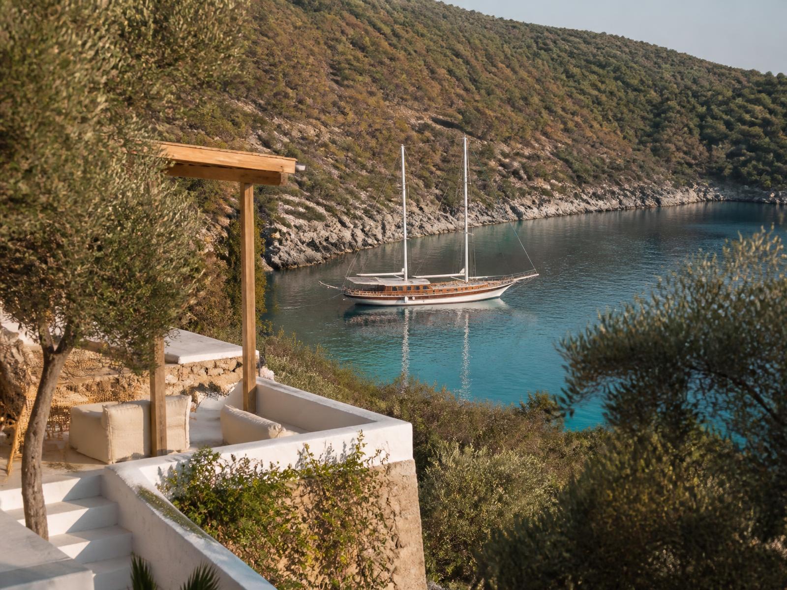 Aegean hillside terrace in Bodrum with whitewashed stone, olive trees and a wooden gulet moored in a turquoise bay