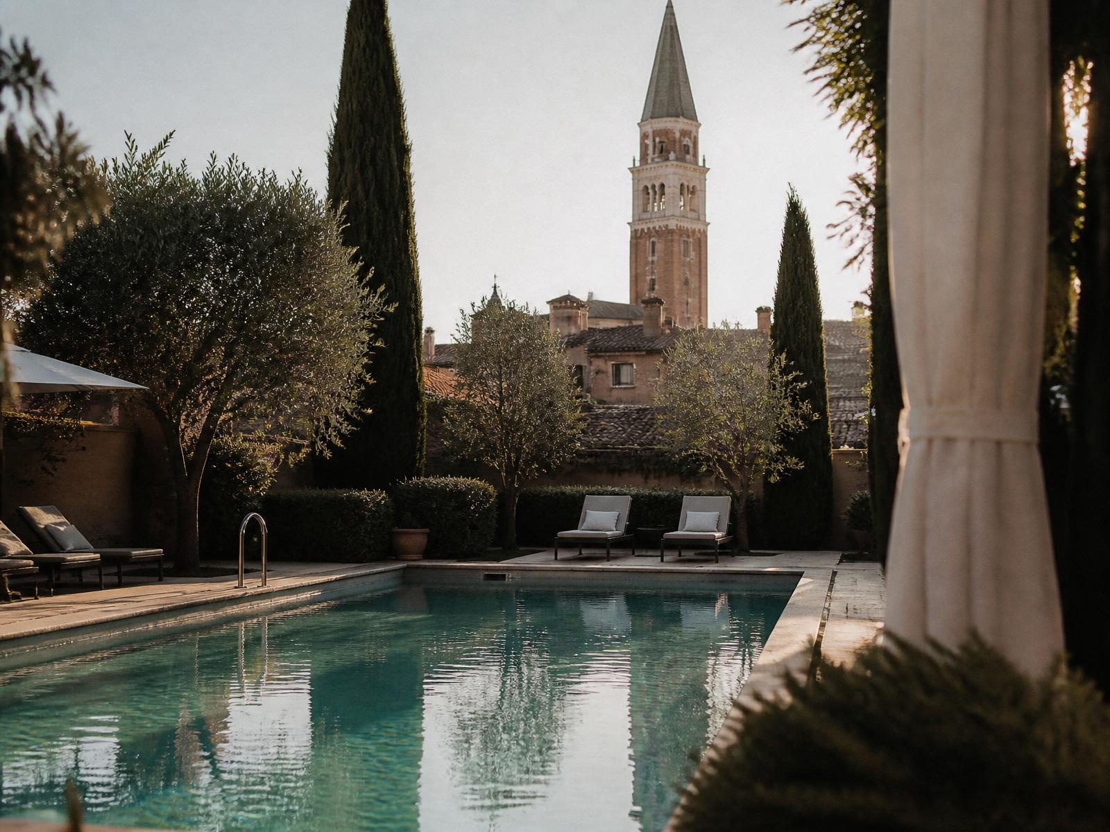 Garden swimming pool framed by cypress and olive trees with a Venetian brick campanile beyond at golden hour
