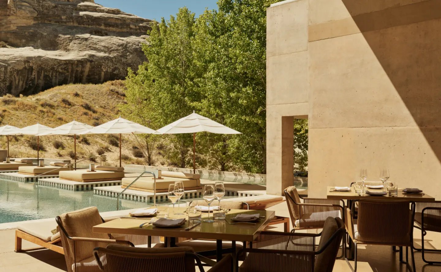 Gedeckte Tische auf der Terrasse des Restaurants von Amangiri direkt am Pool, dahinter Sonnenschirme, Pappeln und die Felswand des Canyons
