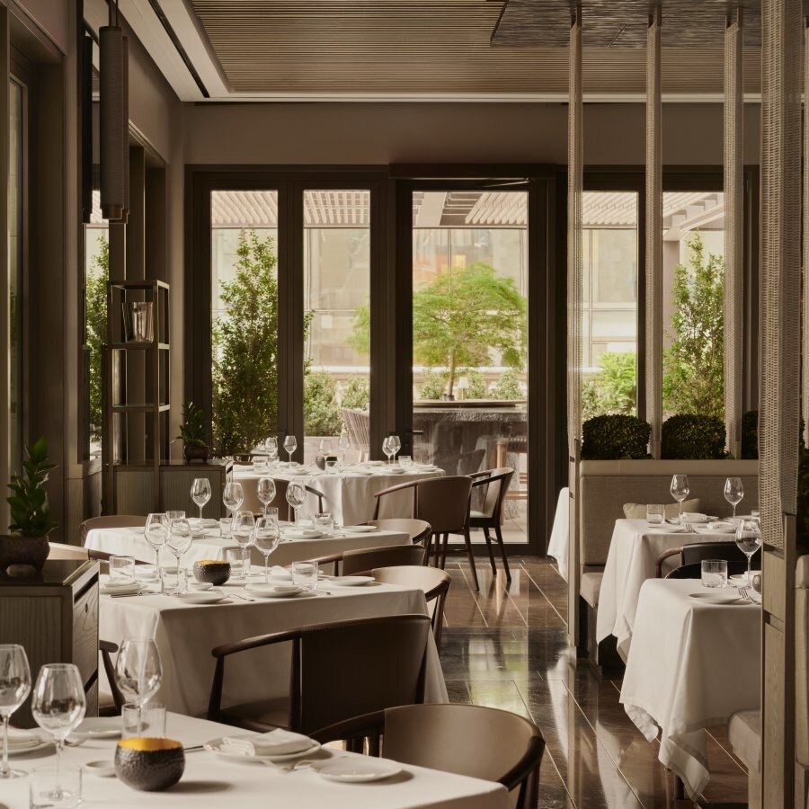 Der Speisesaal des Arva mit weiß eingedeckten Tischen, dunklem Holz und bepflanzten Fenstern zur Terrasse