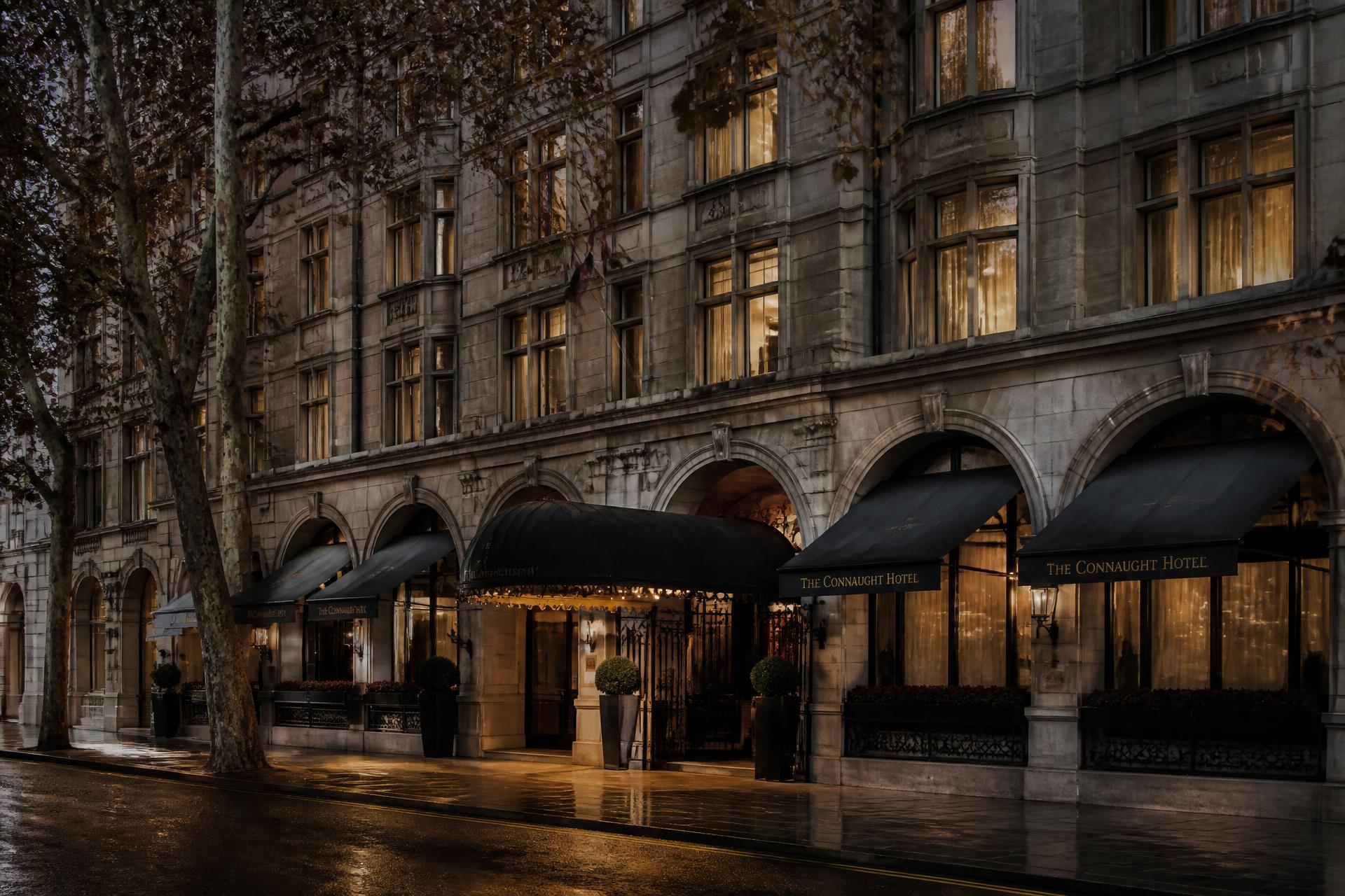 Fassade eines klassischen Grand Hotels in London bei Dämmerung mit Markisen, warm erleuchteten Fenstern und regennasser Straße