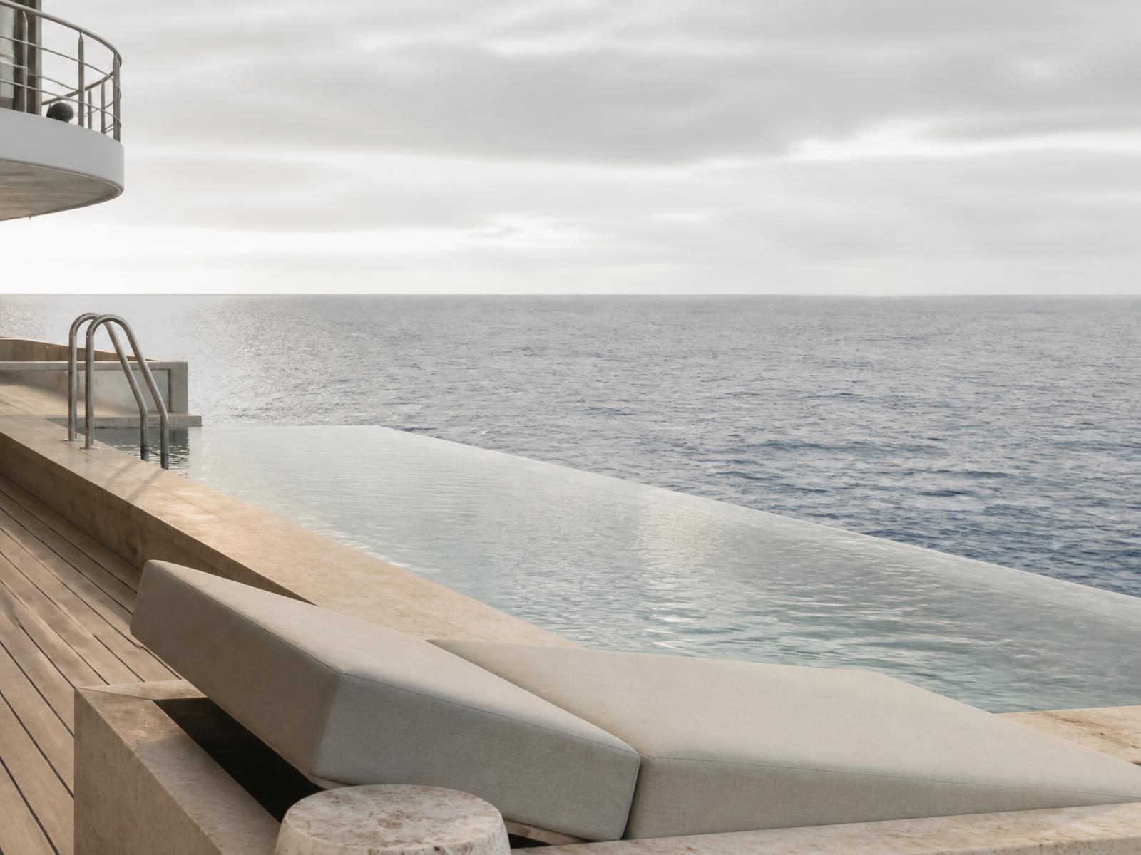 Modern ship deck with an infinity pool and travertine surround facing an open ocean horizon in soft light