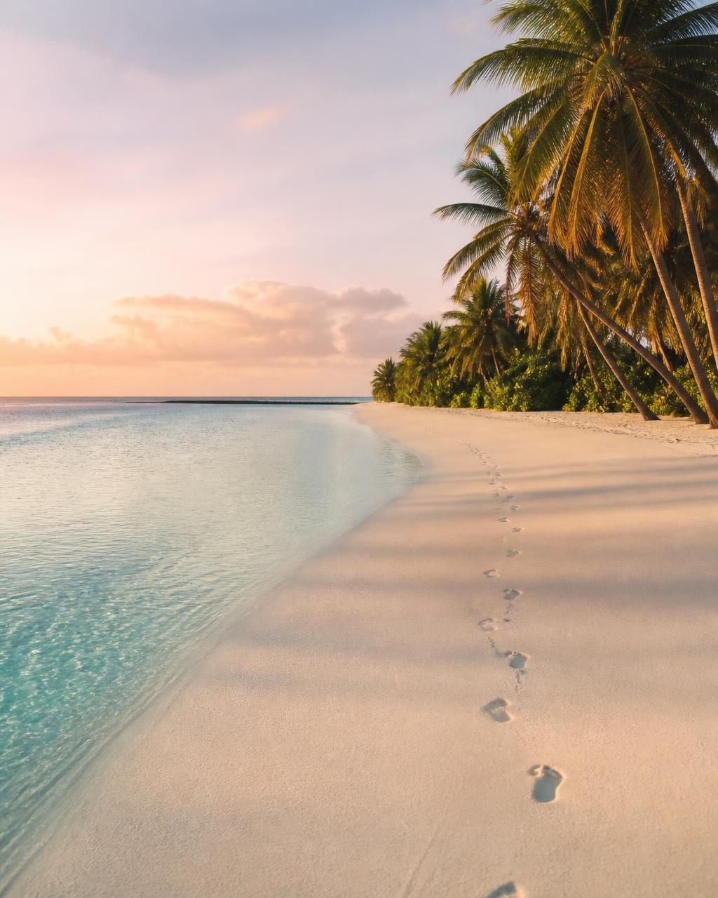 Empty white coral sand beach at sunrise on the Tetiaroa atoll with a single line of footprints and a glassy turquoise lagoon