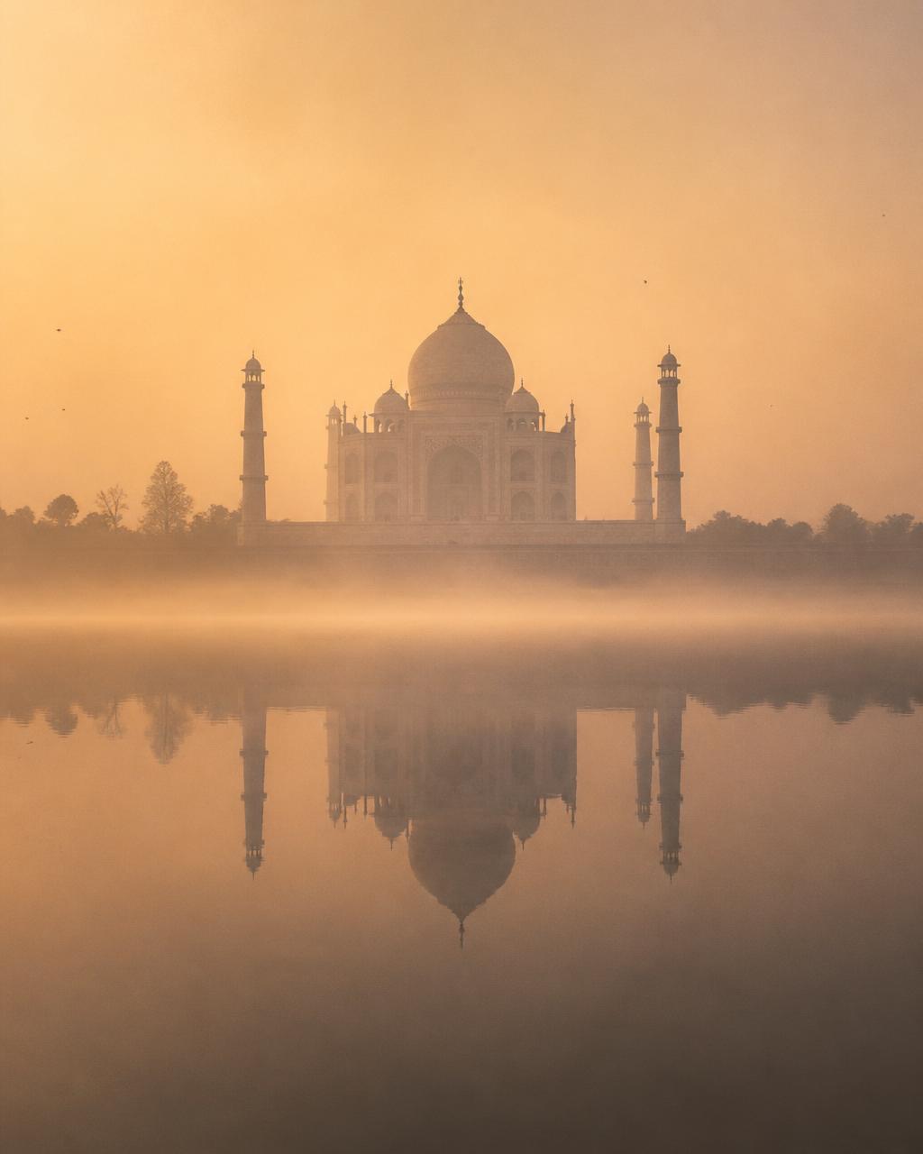 The Taj Mahal at first light, pale marble held in golden mist above the still water of the Yamuna