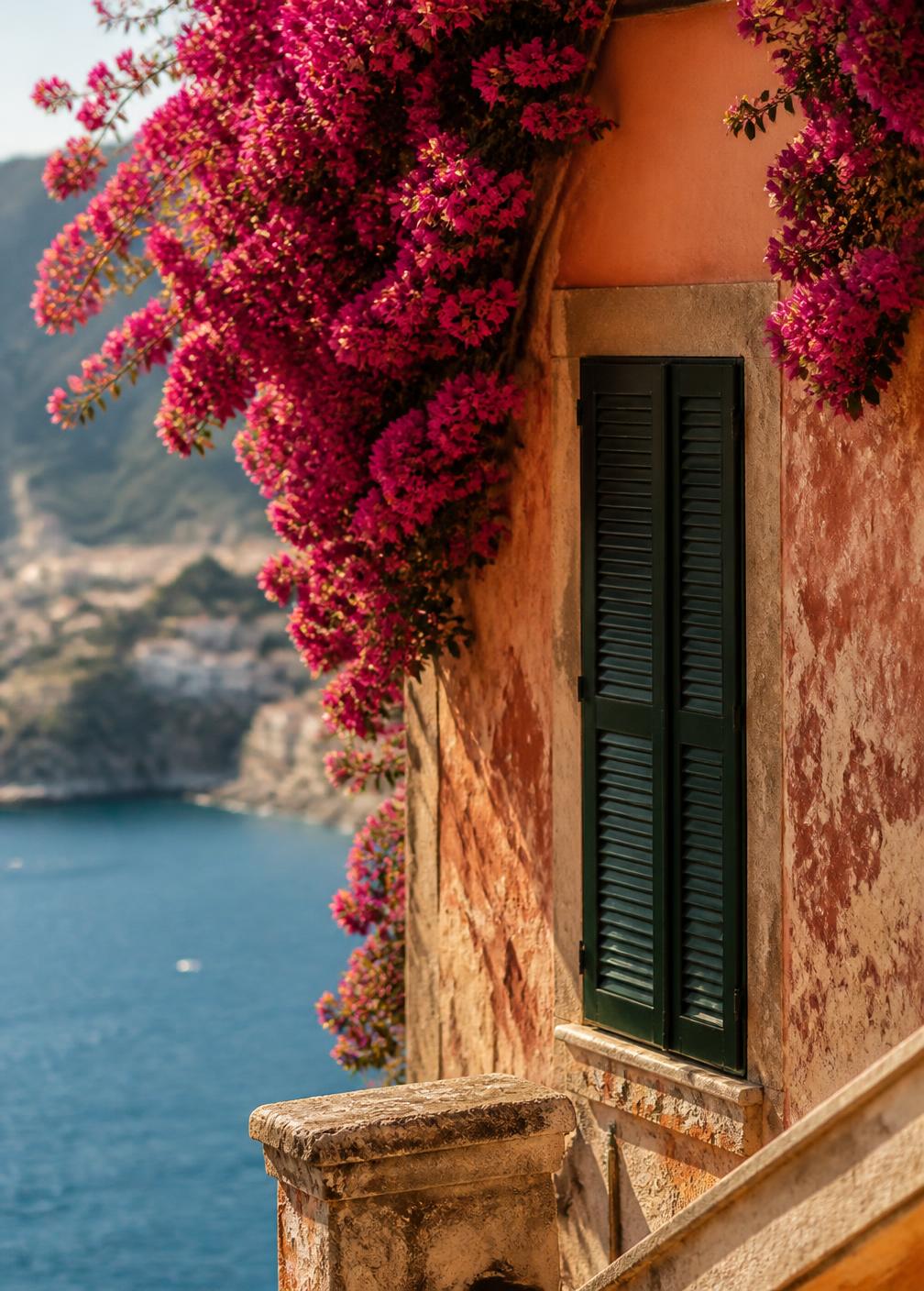 Magenta bougainvillea spilling over a weathered terracotta wall with a green Italian shutter and the Mediterranean beyond