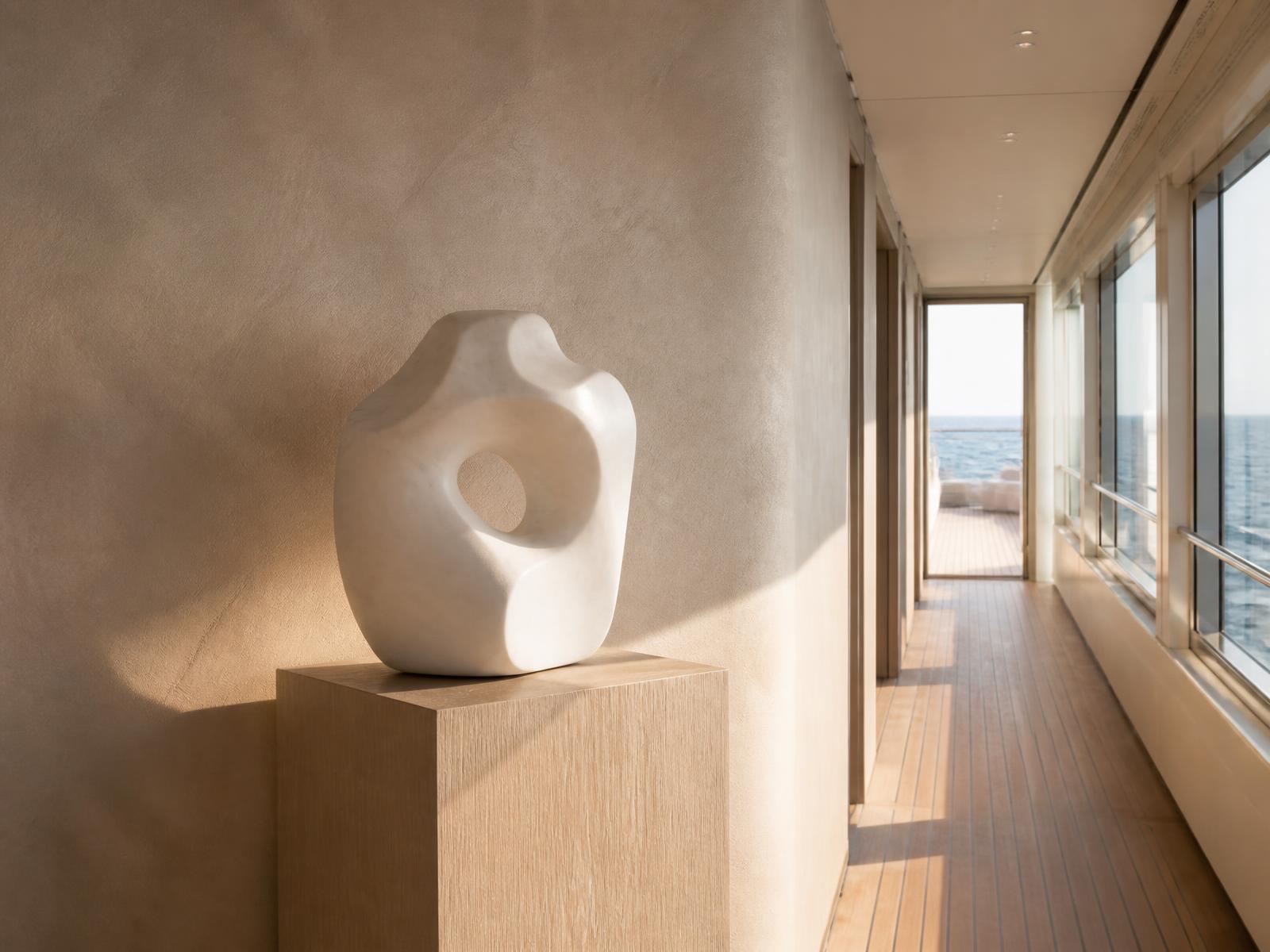 Minimal white sculpture on a pale oak plinth in a sunlit corridor with lime-plaster walls aboard a yacht