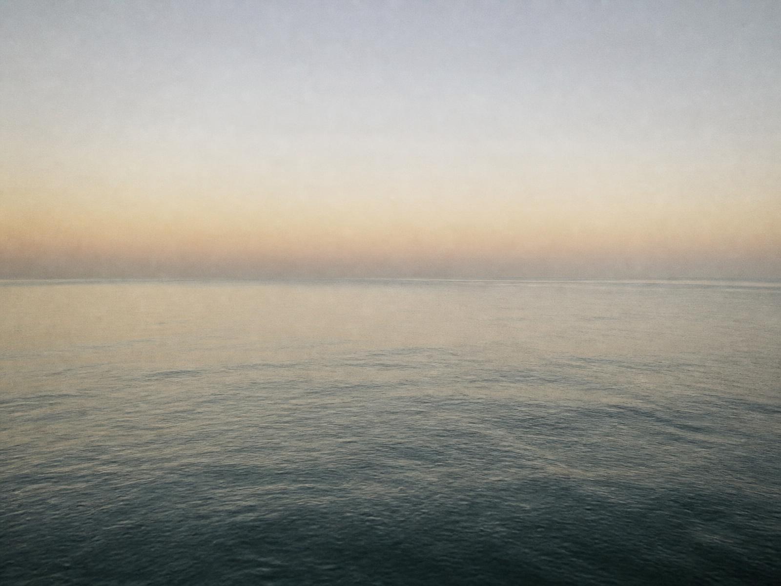 Flat calm ocean horizon at dawn in pale grey and warm cream