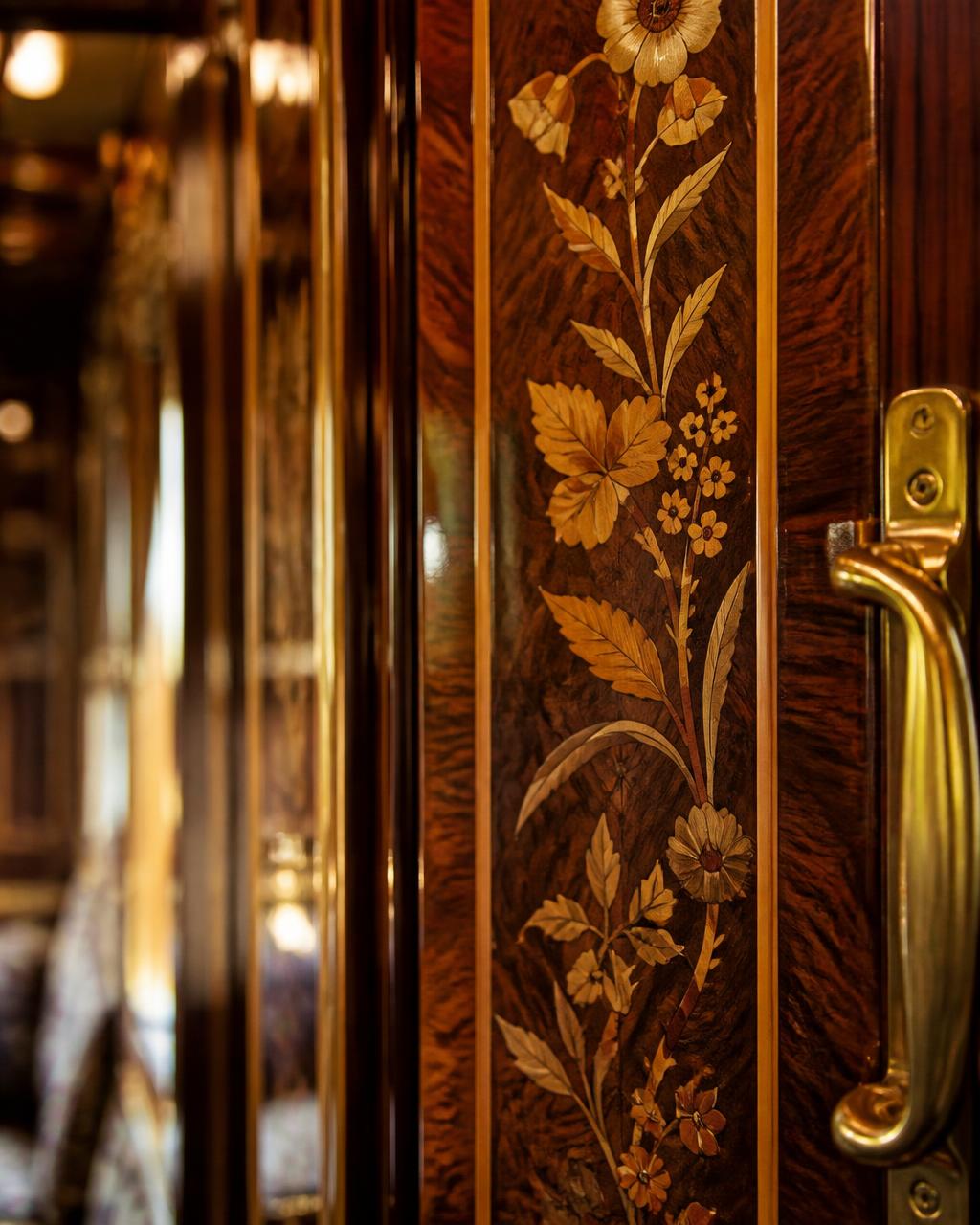 Close detail of 1920s floral marquetry inlay and a polished brass handle on a restored luxury train carriage panel