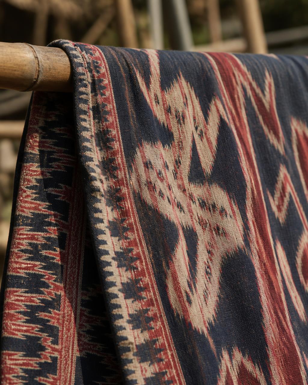 Detail of a hand-woven Sumbanese ikat textile in indigo and morinda red drying on a bamboo rail