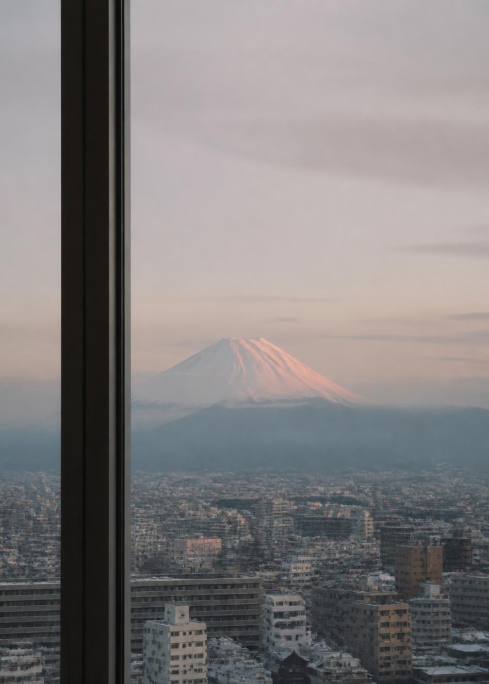 Snow-capped Mount Fuji on the horizon above a pale winter Tokyo skyline seen through a window frame