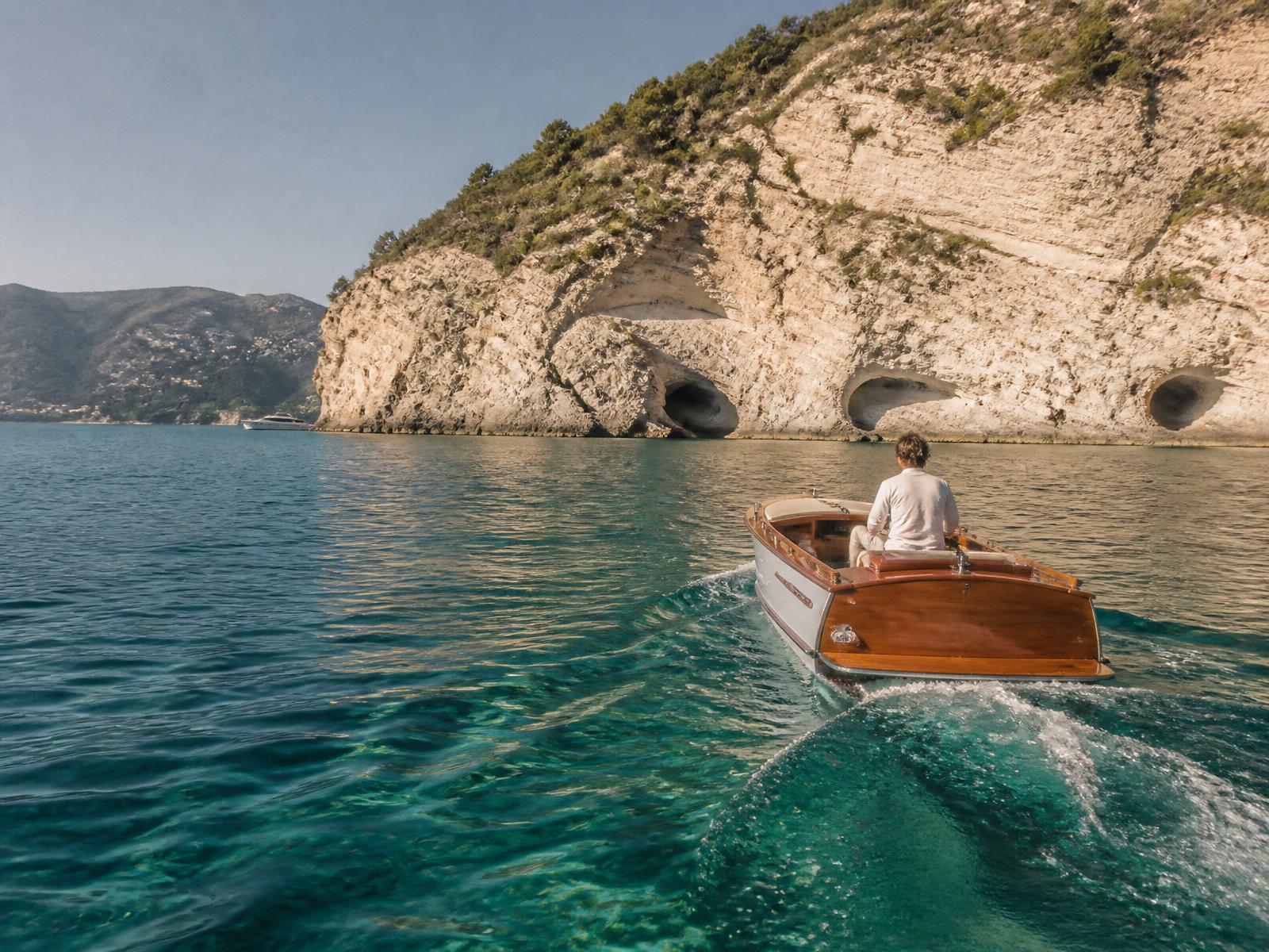 A wooden tender crossing clear turquoise water towards pale limestone cliffs