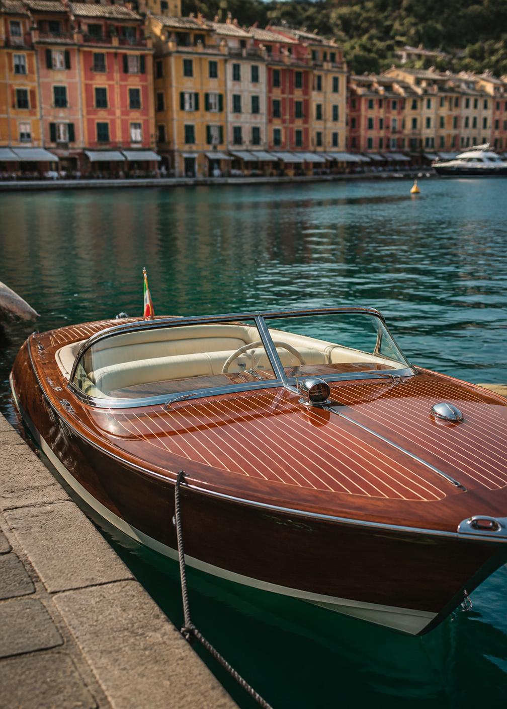 Classic varnished mahogany Riva speedboat moored at a stone quay in Portofino with pastel façades behind