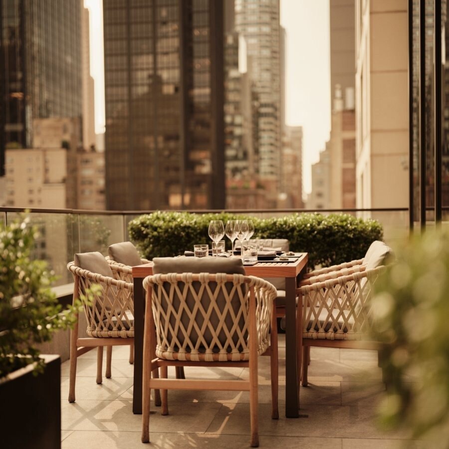 Ein Tisch am Terrassengeländer mit Weingläsern, dahinter die Türme von Midtown im warmen Nachmittagslicht