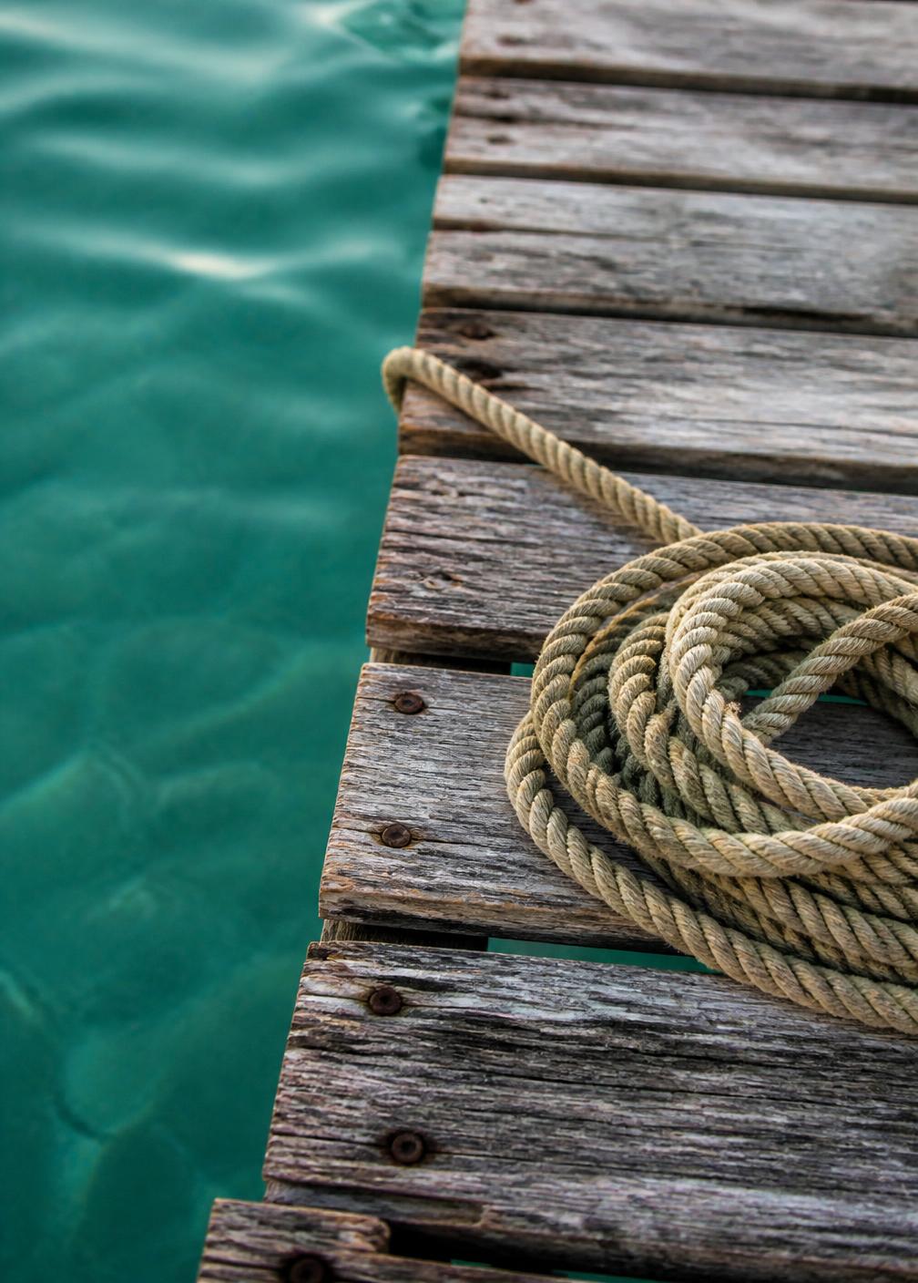 Weathered timber jetty planks with a coiled rope above clear turquoise water