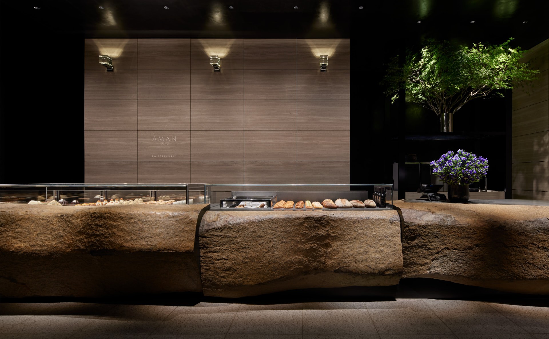 La Patisserie: beleuchtete Vitrine auf einem massiven Findling vor einer Steinwand im abgedunkelten Raum