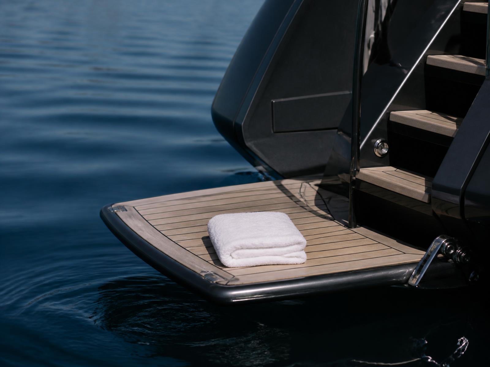 Teak swim platform at the stern of a dark yacht just above deep blue water with a folded white towel