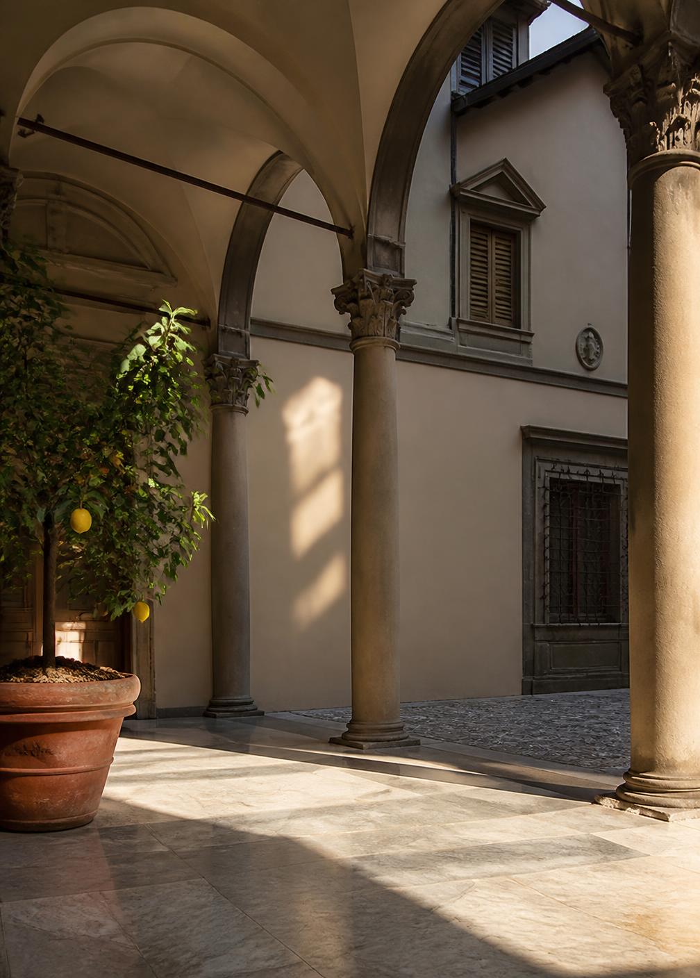 Arched loggia of a Florentine courtyard with slender stone columns, marble floor and a lemon tree in a terracotta pot
