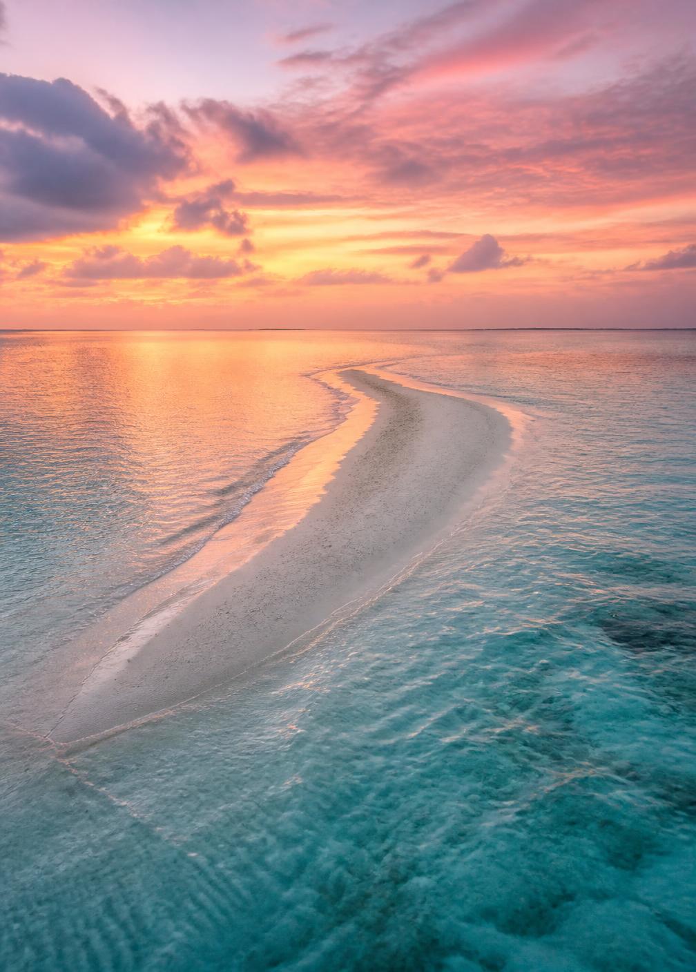 A deserted sandbank in the Indian Ocean at sunset surrounded by turquoise water and a pink sky