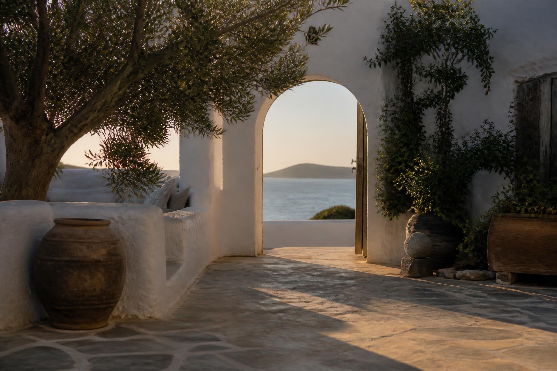 Whitewashed Mediterranean courtyard with an arched doorway opening to the sea at golden hour