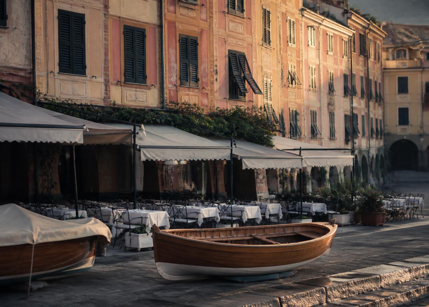 Pastel façades and empty café tables of the Portofino piazzetta in early morning light with a wooden fishing boat on the quay