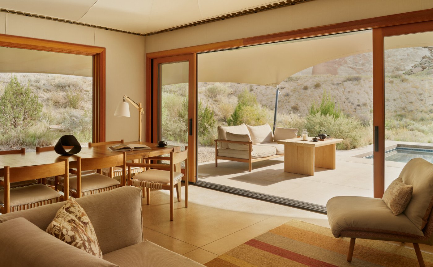 Wohnbereich eines Mesa Pavilion im Camp Sarika mit hellem Holztisch, Leinensofa und geöffneter Schiebetür zur Terrasse mit Pool