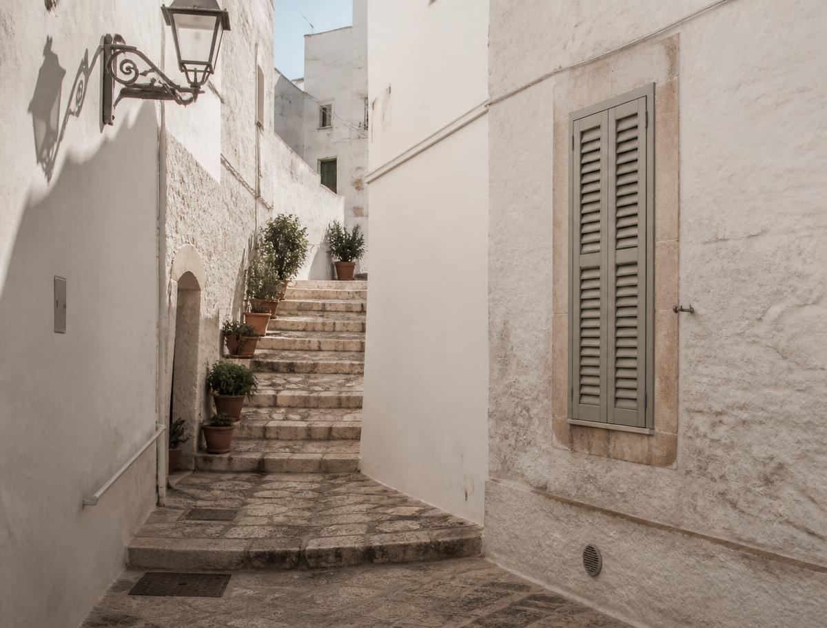 Sunlit whitewashed alley with stone steps and potted plants in a Puglian village