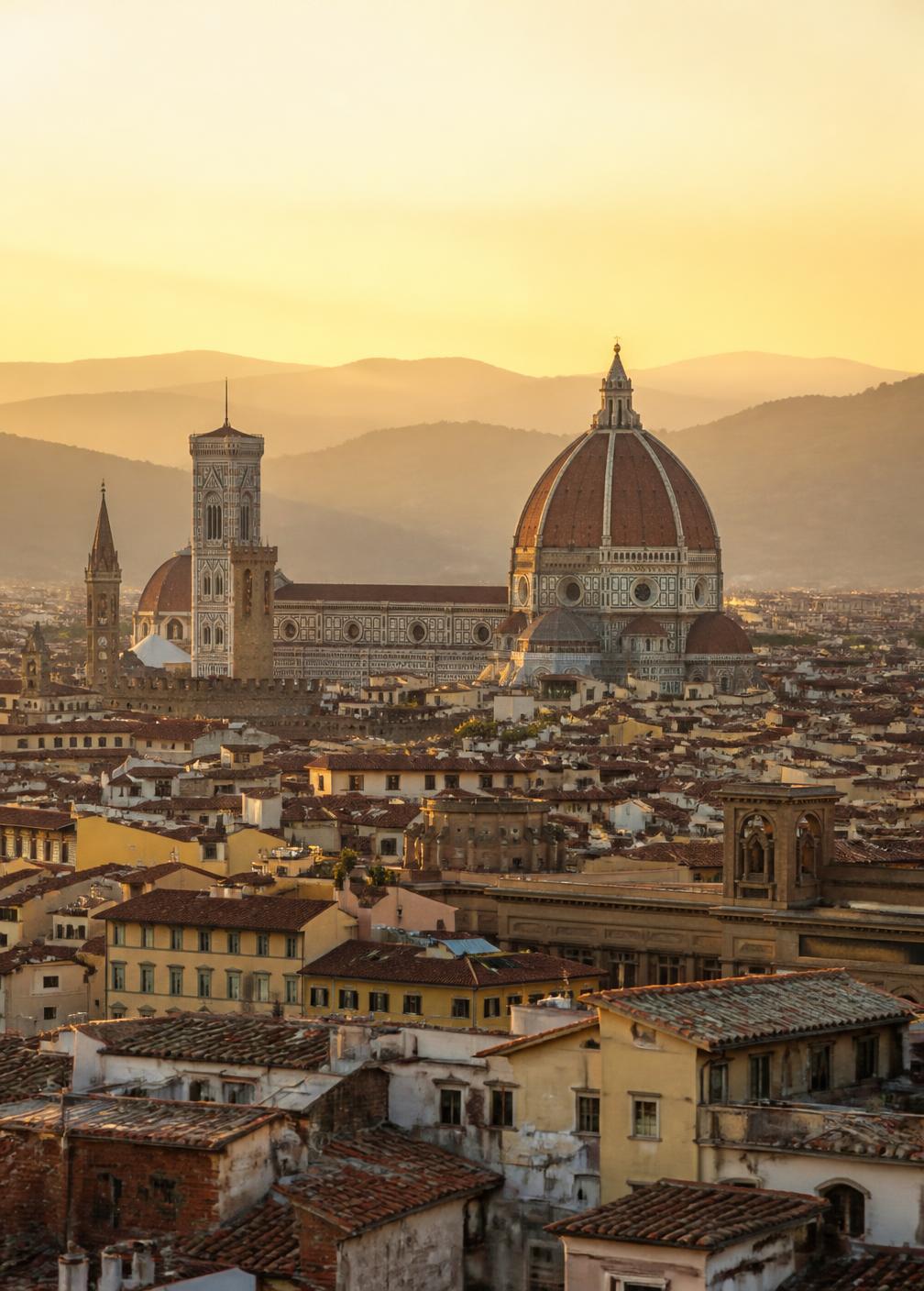 Terracotta rooftops of Florence at dawn with the cathedral dome and bell tower in warm haze