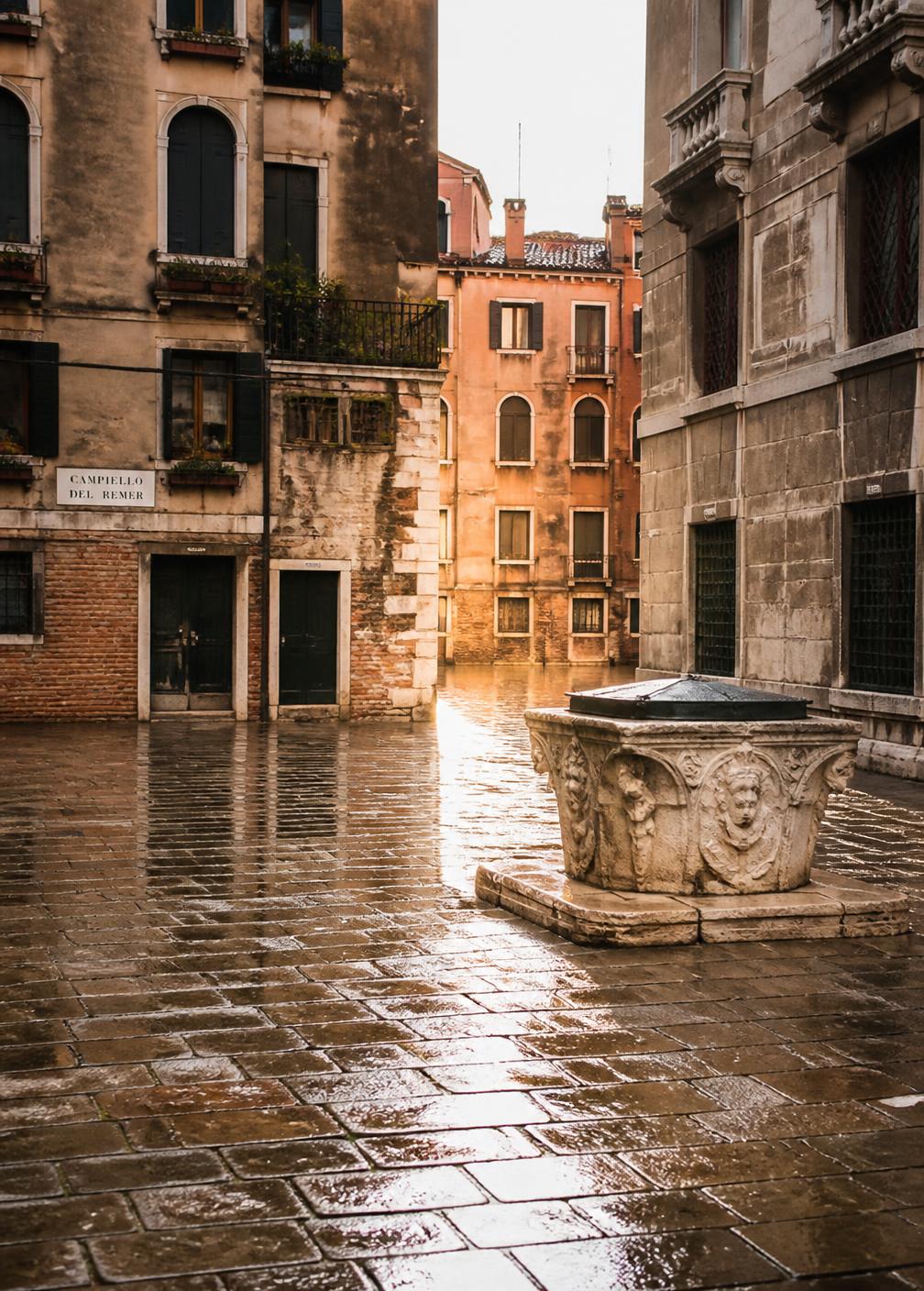 Empty Venetian campo at dawn with wet stone paving and a carved stone wellhead