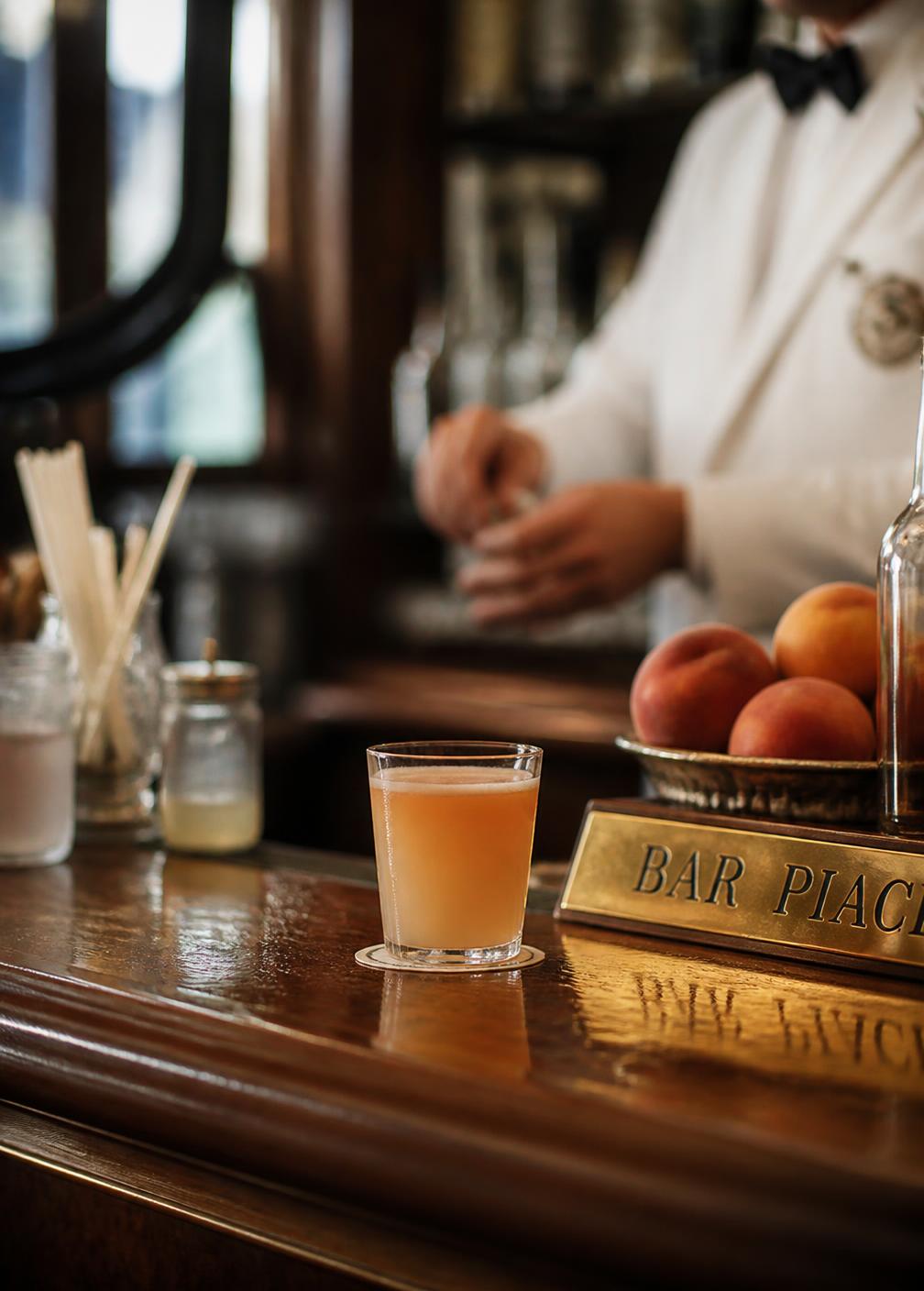 Vintage Italian bar counter with a peach bellini in a small tumbler and a barman in a white jacket behind