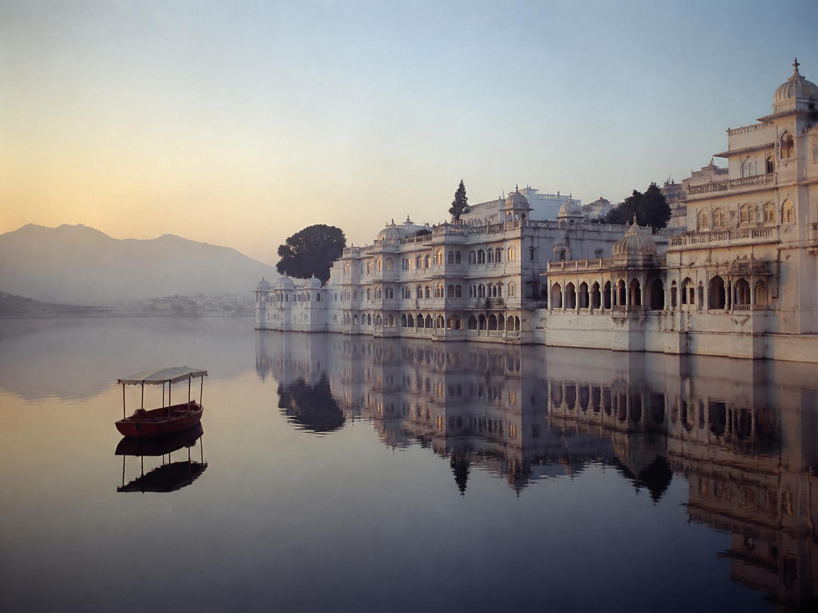 White palaces reflected in the still lake at Udaipur at dawn, a single wooden boat crossing the water
