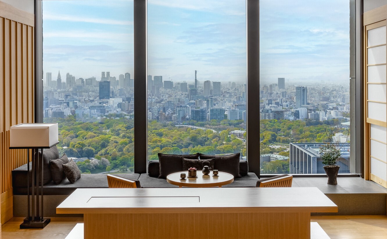 Blick aus einem Zimmerfenster über die Baumkronen eines Parks auf die weite Skyline Tokios