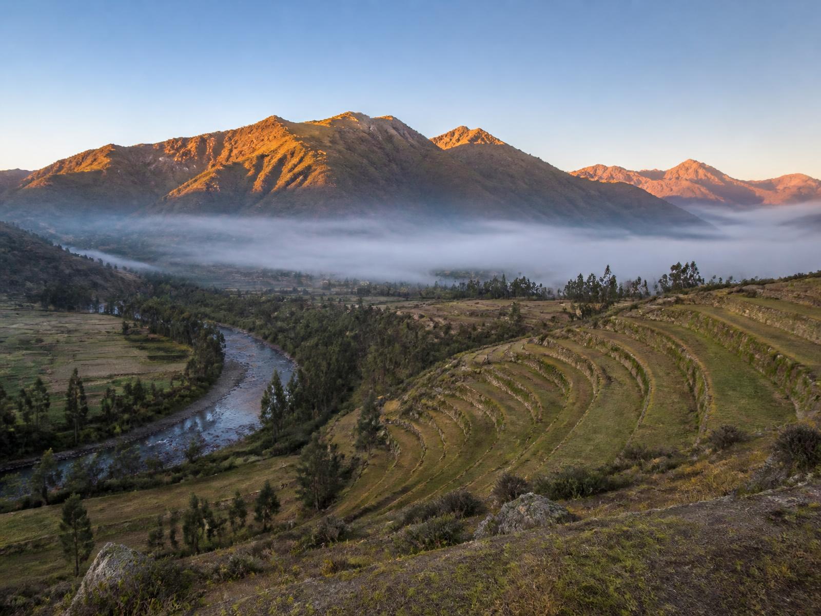 Das Heilige Tal Perus im Morgengrauen mit Inka-Terrassen, einem Fluss und Nebel unter Bergen im ersten Licht