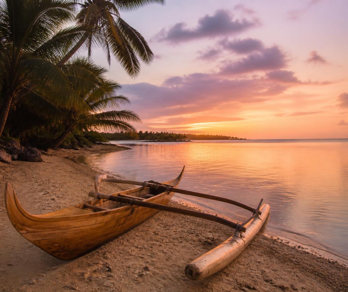 A traditional Polynesian outrigger canoe resting on white sand beside a calm lagoon at dusk