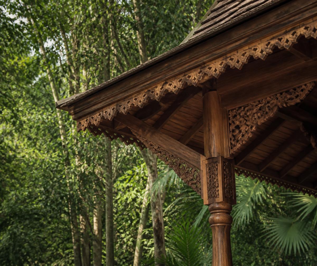 Hand-carved Malaysian timber joinery on a tropical pavilion roof against dense green jungle