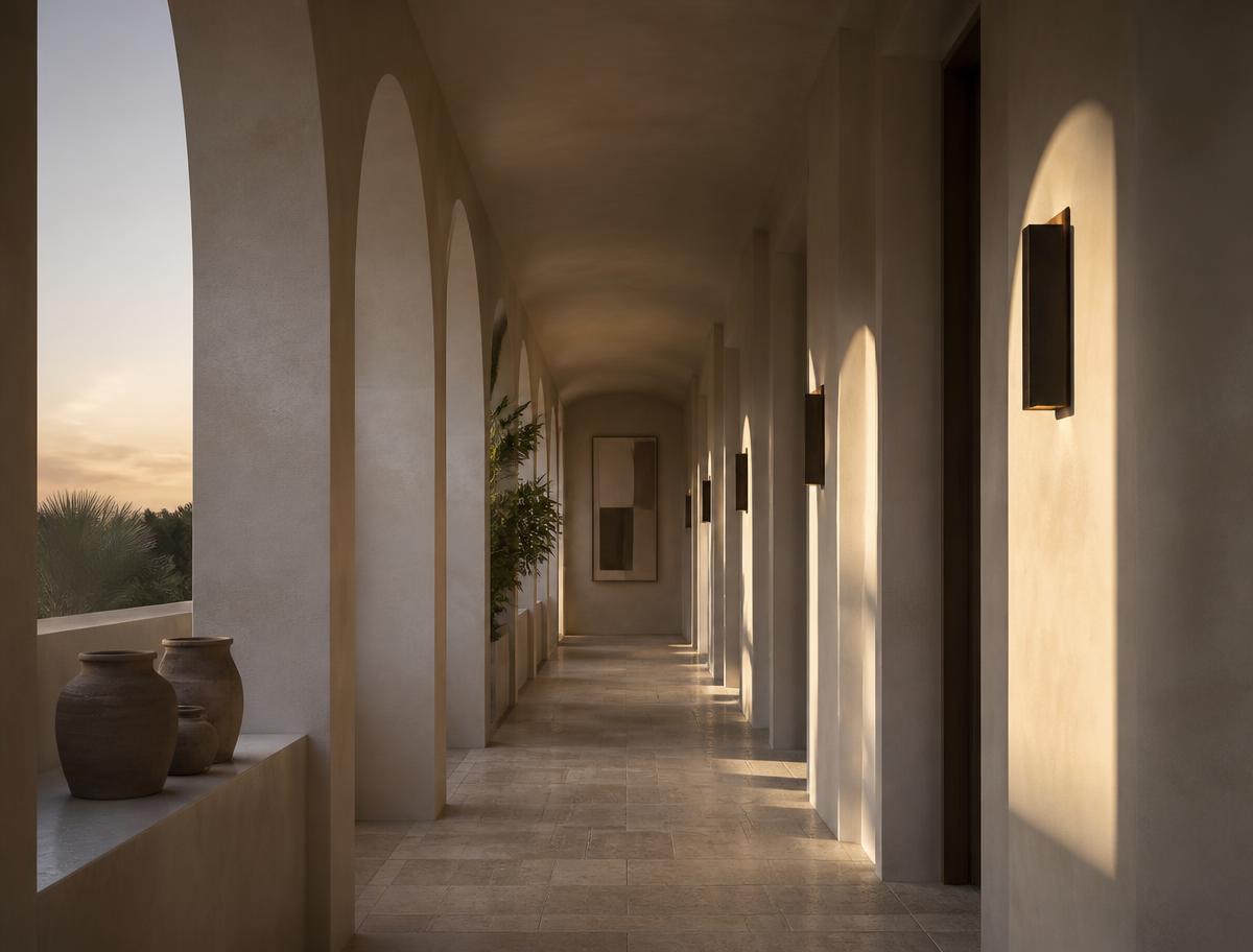 Empty arched hotel corridor in warm plaster with long shadows at dusk