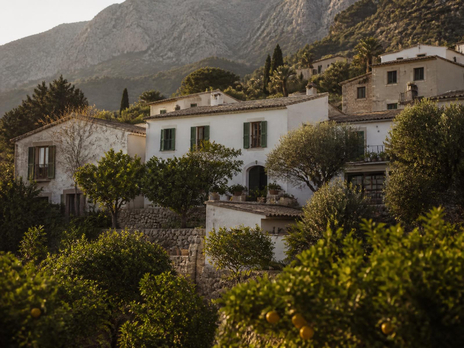 Whitewashed Mallorcan manor houses with green shutters among terraced citrus and olive groves below the Tramuntana