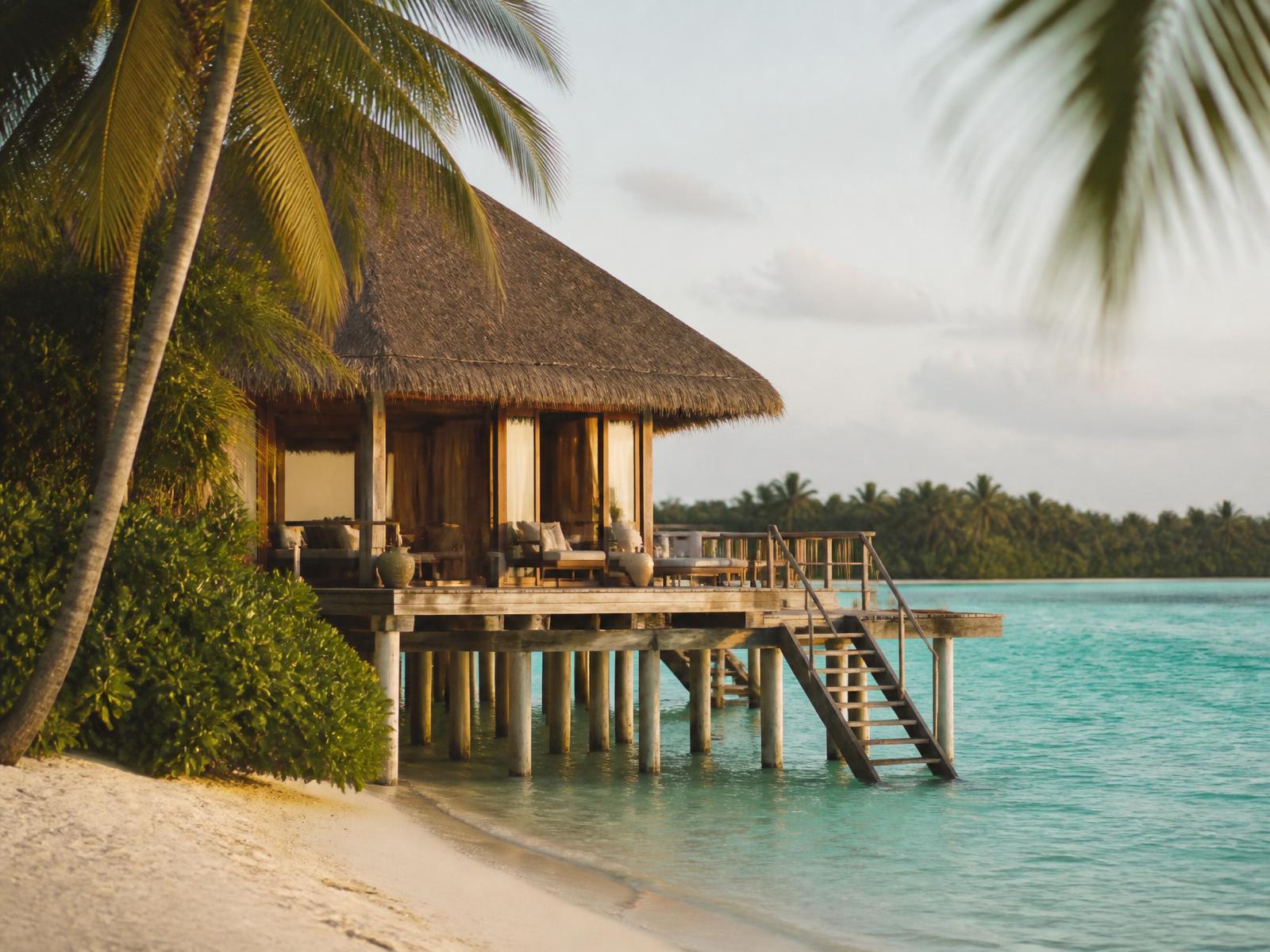 Thatched timber overwater villa on stilts above a turquoise Maldivian lagoon at golden hour