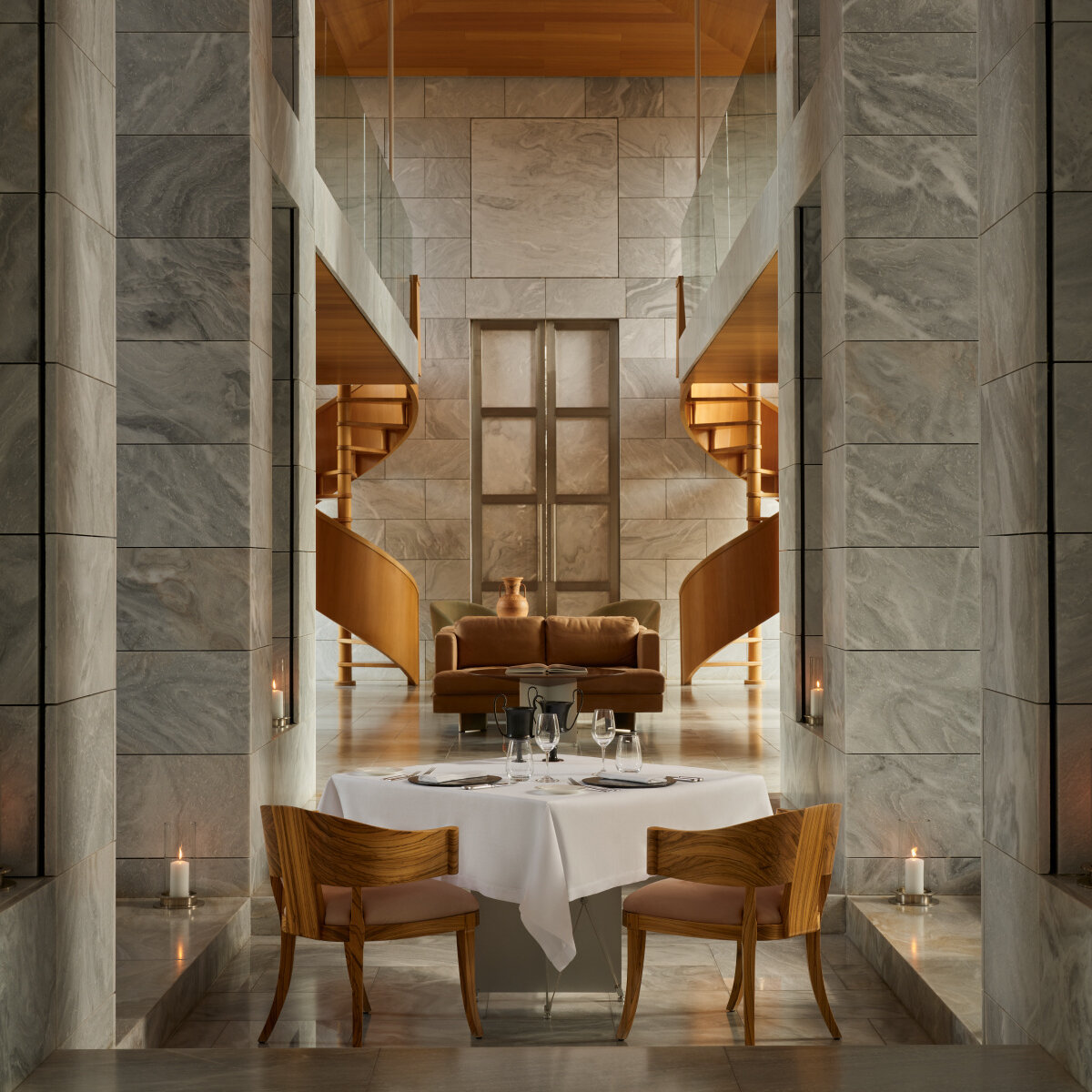 Privates Dinner in der Bibliothek von Amanzoe: ein gedeckter Tisch zwischen hohen Marmorwänden, Kerzen auf den Stufen und zwei hölzerne Wendeltreppen im Hintergrund