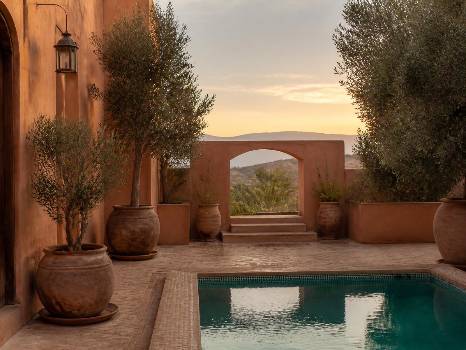 Moroccan riad villa courtyard in Marrakech with ochre earth walls, olive trees and a still turquoise pool at golden hour