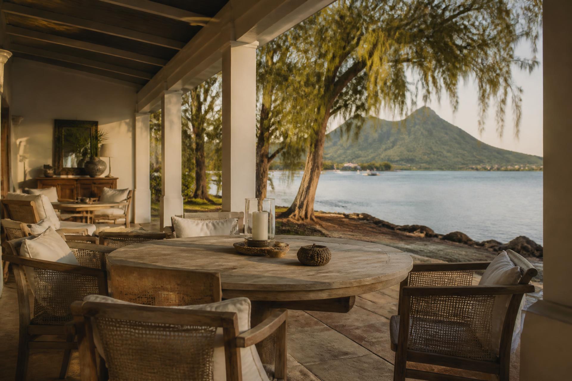 A veranda with teak furniture and linen above a Mauritian lagoon in afternoon light