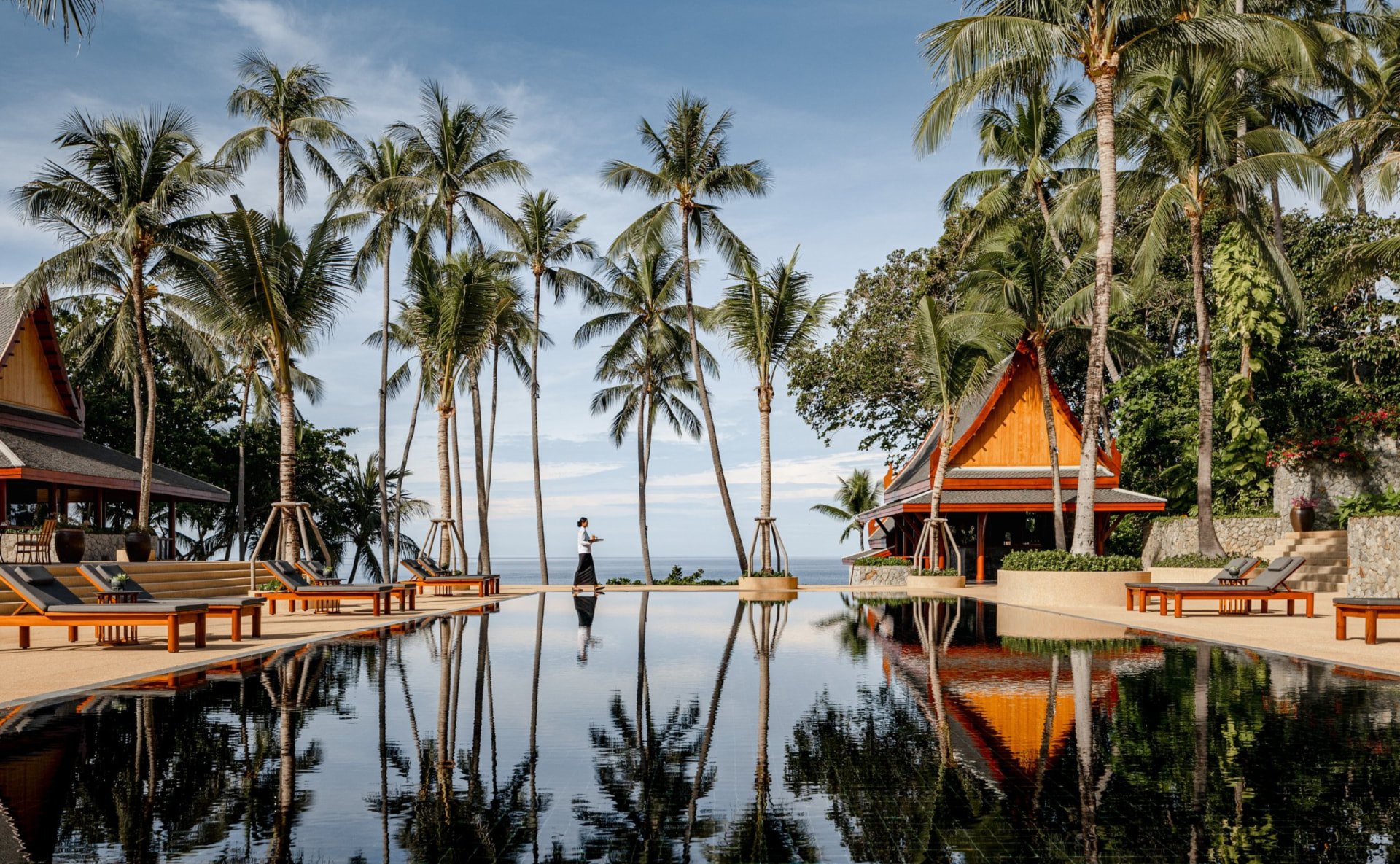 Der schwarze Hauptpool des Amanpuri, gesäumt von hohen Kokospalmen und thailändischen Pavillons, im Mittagslicht