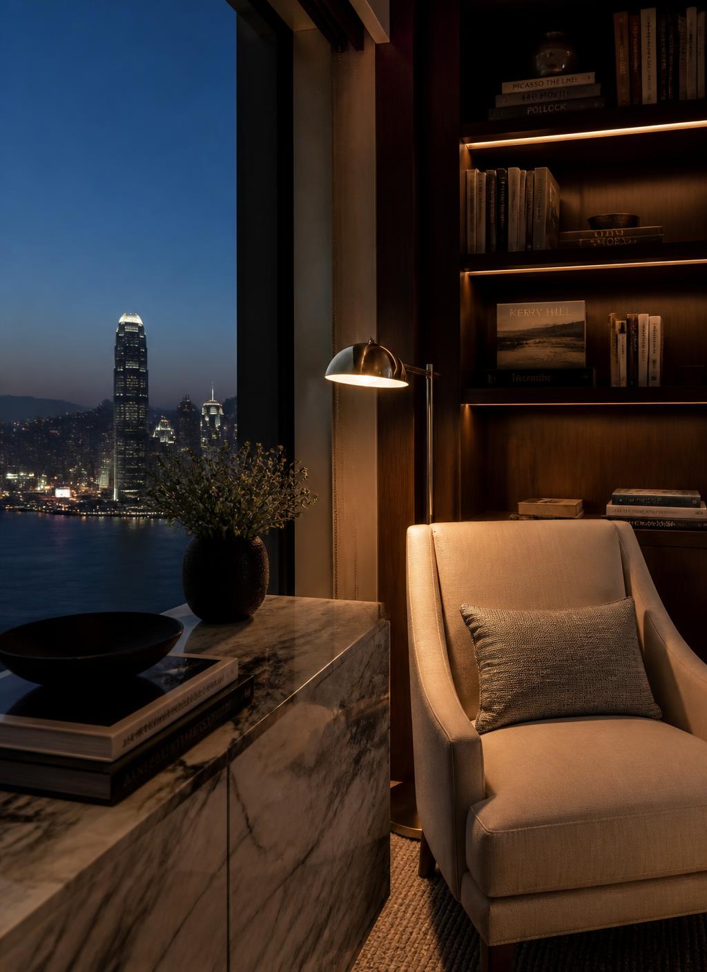 Private library corner of a Hong Kong hotel suite at dusk with oak shelves of art books, a bronze reading lamp, a linen armchair and harbour lights beyond the window
